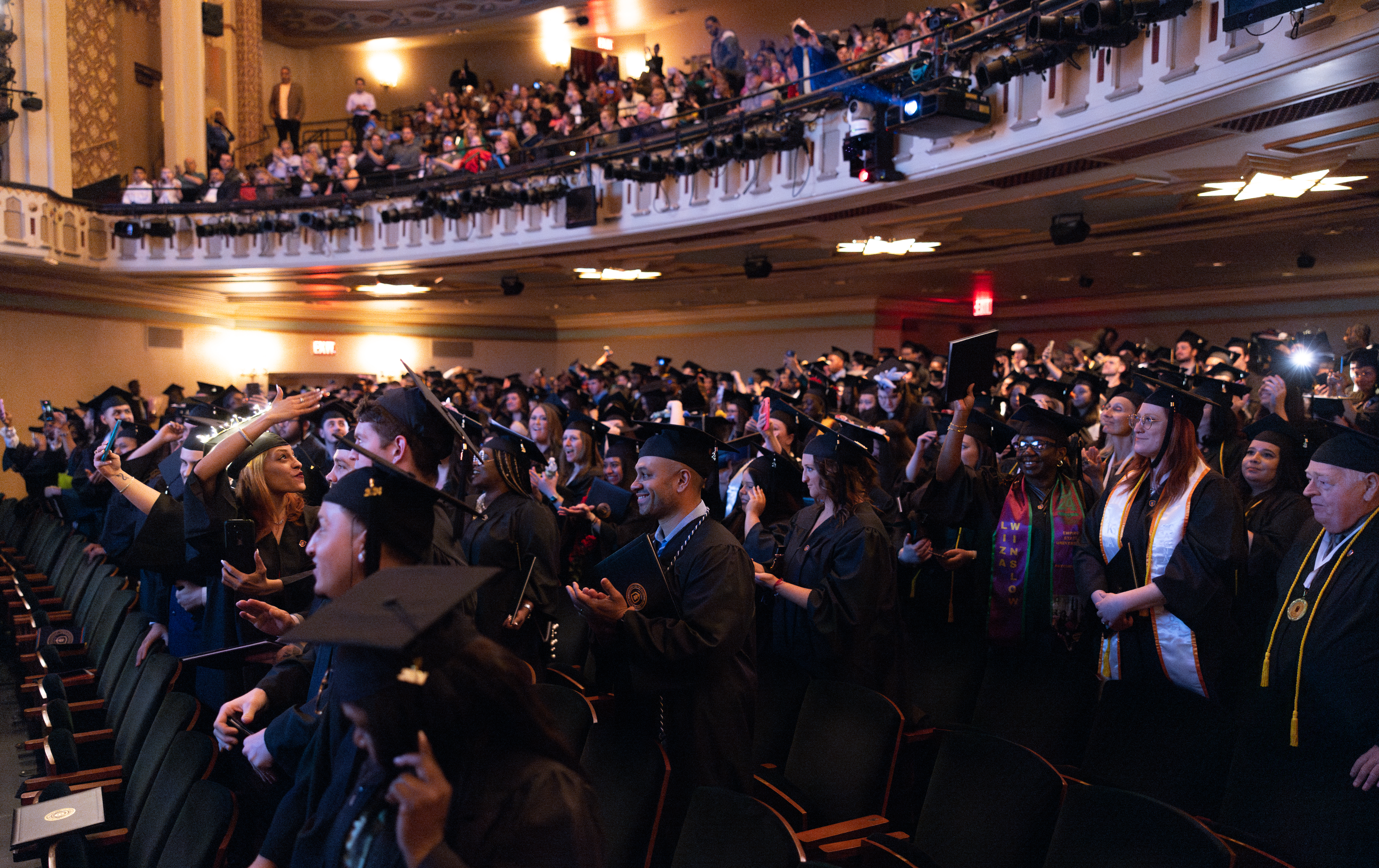 group of students in auditorium in caps and gowns celebrating